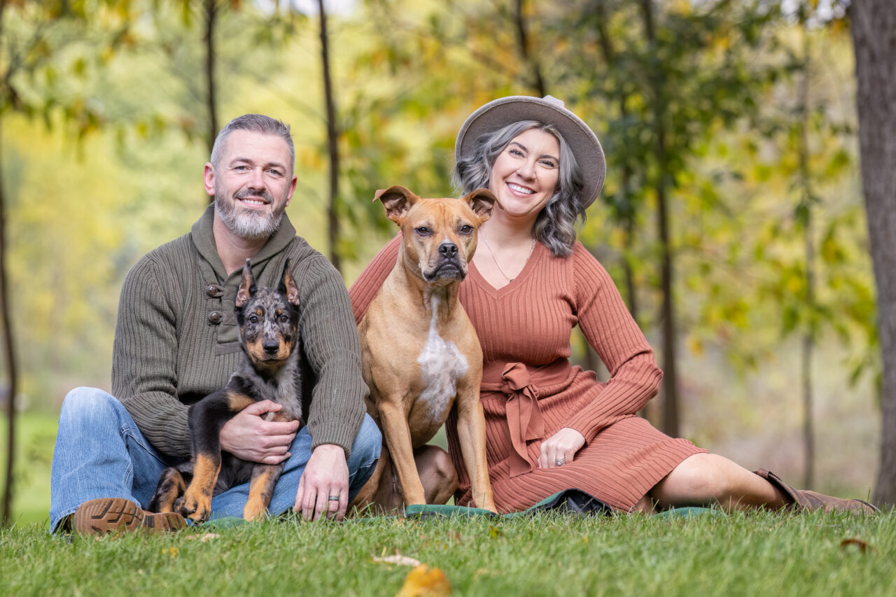 A couple sits in the grass outside of their house in Ada, Michigan with their two dogs.